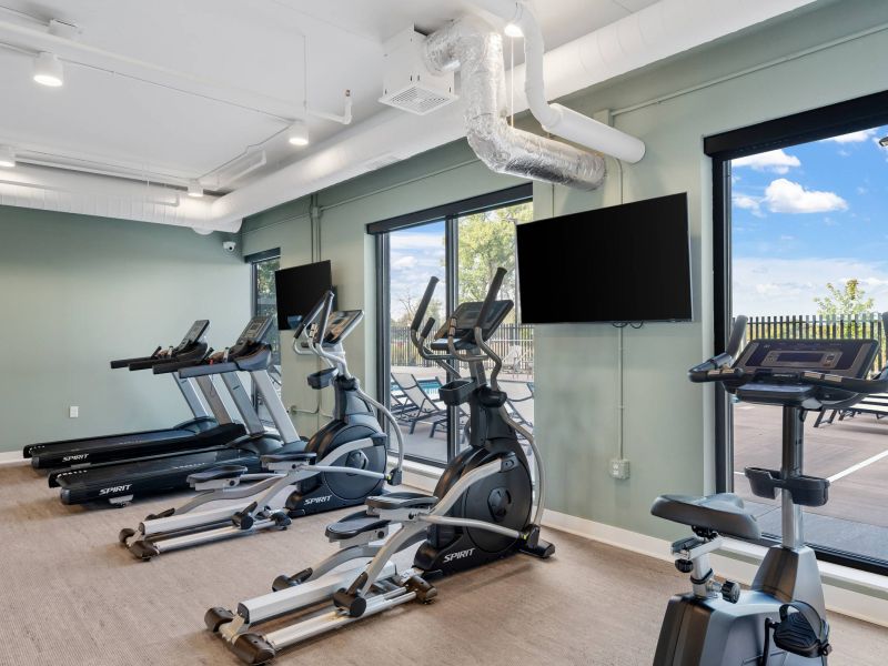 Lexi Apartments Modern gym with treadmills, elliptical machines, and bikes facing large windows and wall-mounted TVs.
