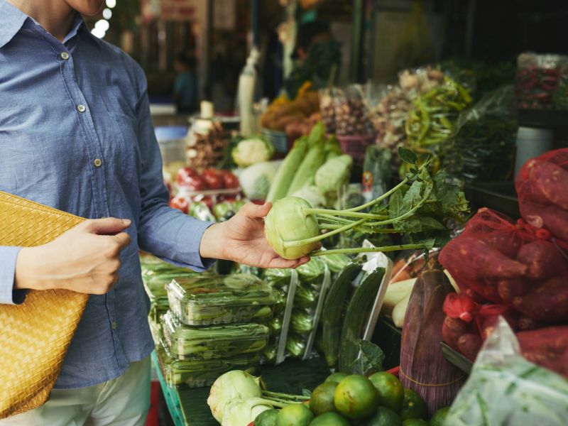 Lexi Apartments Person holding a kohlrabi while shopping for fresh vegetables at a market stall.