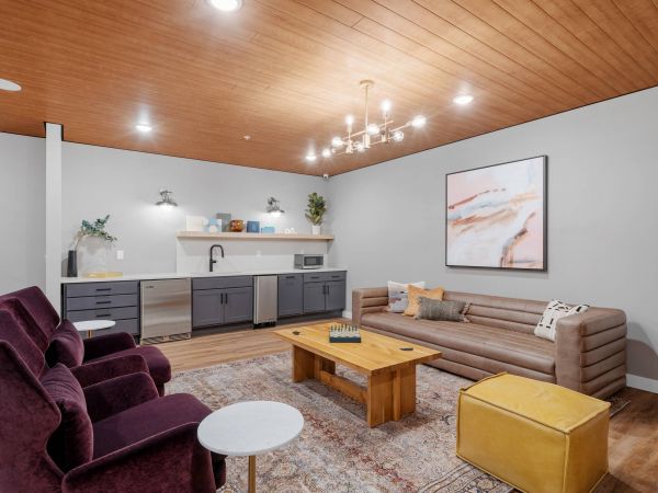 Lexi Apartments Modern lounge with a sofa, velvet chairs, coffee table, kitchenette, and wall art under warm lighting.