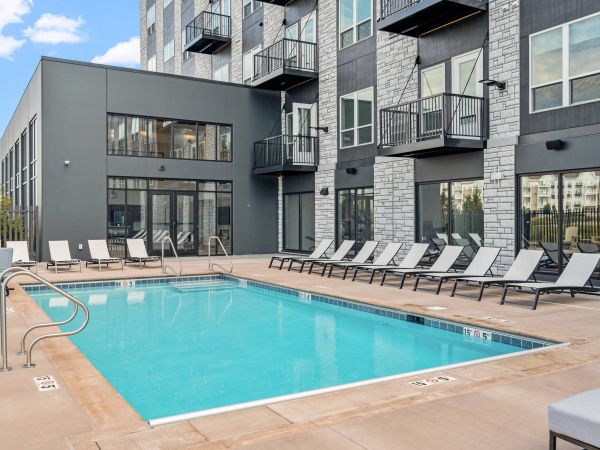 Lexi Apartments Outdoor pool surrounded by lounge chairs at a modern apartment complex with balconies and large windows.