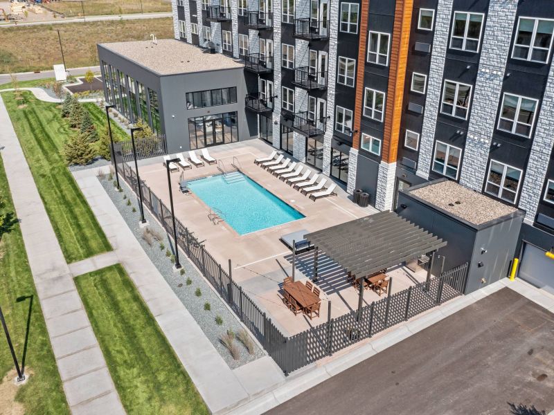 Lexi Apartments A modern apartment building with a rectangular outdoor pool, lounge chairs, and a shaded seating area.