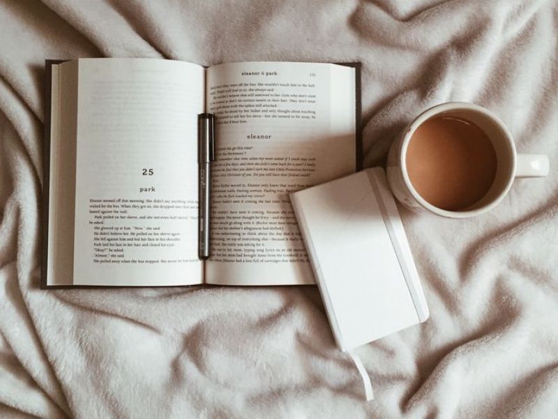 Lexi Apartments Open book, notebook, and a cup of coffee on a soft beige blanket, creating a cozy reading scene.