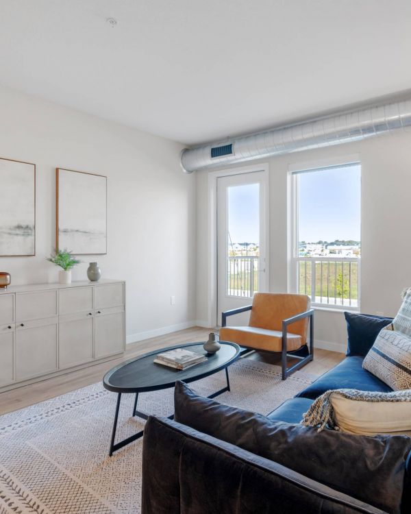 Lexi Apartments Modern living room with a blue sofa, armchair, coffee table, and large windows letting in natural light.