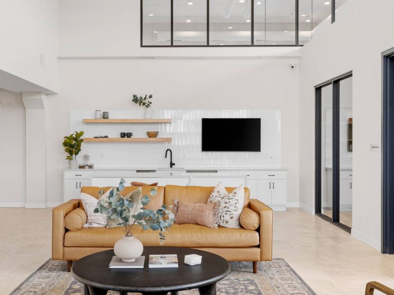Lexi Apartments Modern living room with tan sofa, round black coffee table, and minimalist white kitchen in the background.