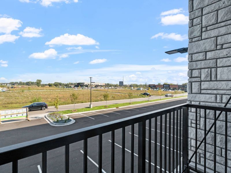 Lexi Apartments View from a balcony overlooking a parking lot, road, and grassy field under a blue sky with clouds.