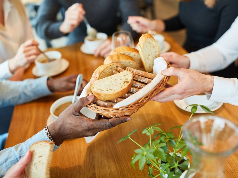 Lexi Apartments People sitting around a table share a basket of sliced bread, with bowls of soup in front of them.